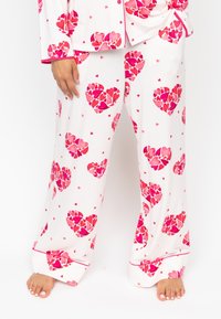 Witte pyjama set met grote rode en roze hartpatronen, met contrasterende roze afwerking. De stof is zacht en glad met een comfortabele pasvorm.