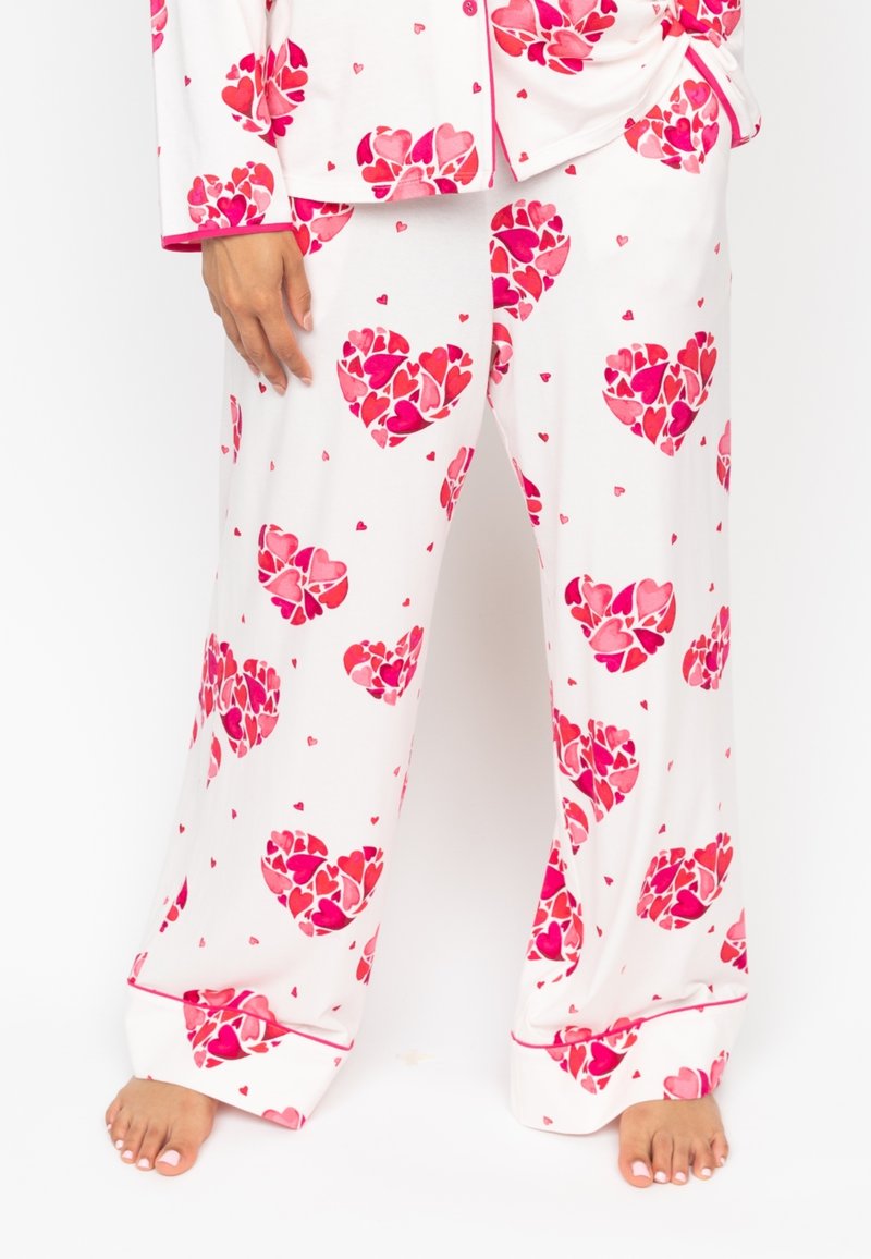 Witte pyjama set met grote rode en roze hartpatronen, met contrasterende roze afwerking. De stof is zacht en glad met een comfortabele pasvorm.