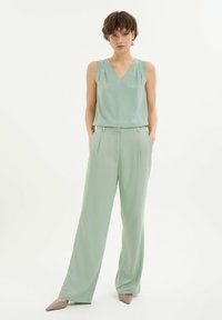 Miętowa bezrękawnikowa bluzka z dekoltem w kształcie litery V, zestawiona z szerokimi miętowymi spodniami. Gładki materiał z delikatnymi detalami plisowania. Wąskie, beżowe buty.
