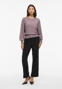 Svjetloplavi pulover s napučenim rukavima i rebrastim rubom, uparen s crnim ravnim hlačama i crnim šiljastim štiklama.