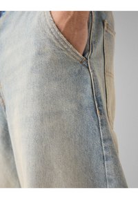 Ljusblå denimjeans med en urtvättad textur, sidoficka och synlig sömnad. Tyget har ett klassiskt twillmönster.