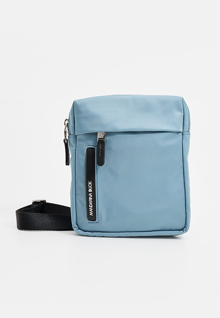 Hellblaues Umhängetäschchen aus weichem Stoff, mit einem Reißverschluss-Hauptfach und einer Vordertasche mit einem schwarzen Logoakzent.