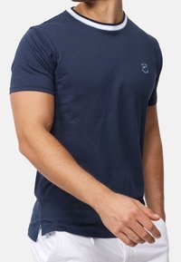 Camiseta de algodón de color azul marino con un cuello redondo de rayas blancas y azules, mangas cortas y un pequeño logo en el pecho. Aberturas laterales en el dobladillo.
