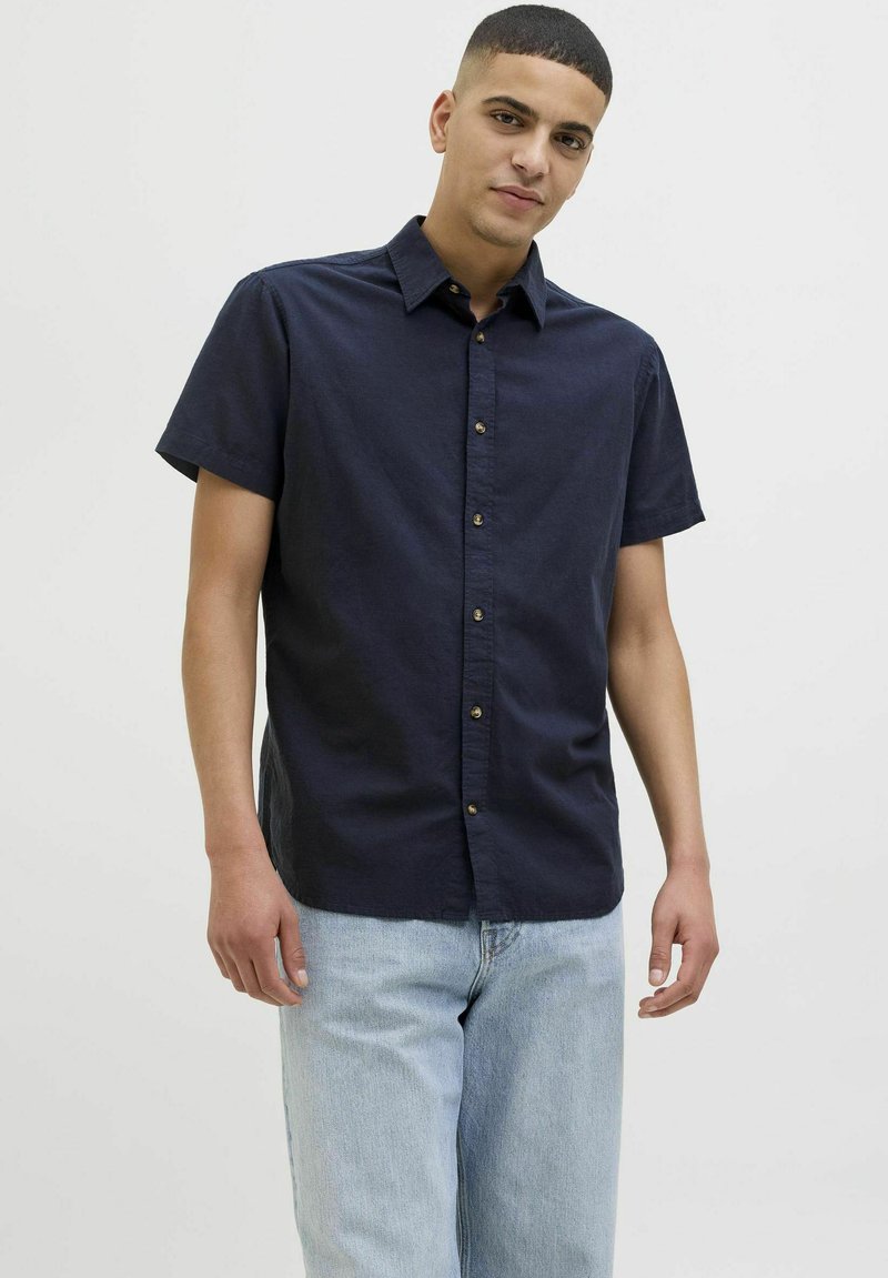 Camisa de botones de manga corta en color azul marino con cuello, que presenta una textura suave y botones dorados en la parte delantera.