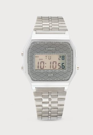 Montre numérique Casio avec bracelet métal argenté, cadran gris à motif, affichant l'heure 10:10:56, la date mardi 28 et indication de résistance à l'eau.