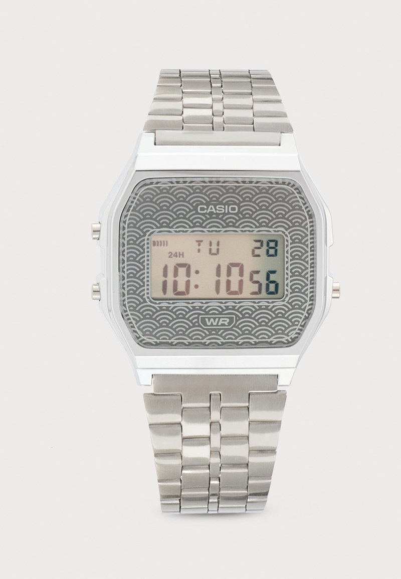 Montre numérique Casio avec bracelet métal argenté, cadran gris à motif, affichant l'heure 10:10:56, la date mardi 28 et indication de résistance à l'eau.