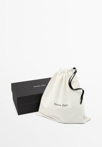 Zwarte rechthoekige Massimo Dutti doos naast een witte stoffen zak met zwarte koorden en het Massimo Dutti-logo aan de voorkant.