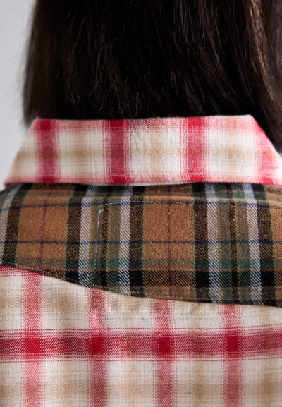 Plaid shirt with contrasting panels; red and beige checkered upper collar, brown and green checked lower back, soft fabric texture.