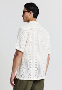 Kurzärmliges, offenes Strickhemd in hellem Creme mit Diamantmustern, ausgestattet mit einem Campkragen und einem lockeren Schnitt. Texturiert, atmungsaktives Material.