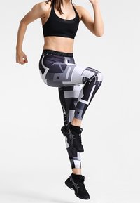 Reggiseno sportivo nero abbinato a leggings geometrici aderenti in bianco e nero. Presenta un materiale elegante con una vita alta e un design a motivi.
