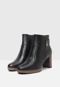 Zwarte leren enkelboots met een gladde afwerking, zijrits en een bruine houten blockheel. Voorzien van subtiele stiksels en metalen accenten.