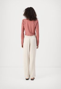 Top de manga larga a cuadros rojos y blancos combinado con pantalones de pierna ancha beige. Los pantalones tienen una cintura elástica y dos bolsillos traseros.