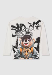 Biała koszula z długim rękawem z grafiką misia w okularach przeciwsłonecznych, czapce, bluzie z kapturem, plecaku i złotych łańcuchach, z czarnym napisem w graffiti.