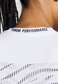 T-shirt de sport blanc avec une texture côtelée au niveau du col et un motif graphique en gris et noir dans la section inférieure.