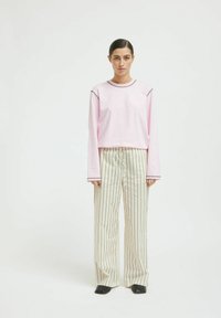 Light pink long-sleeve t-shirt with a contrasting neckline, paired with cream wide-leg striped trousers and black square-toed shoes.