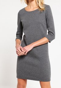 Robe grise texturée avec des manches trois-quarts, un col rond et une coupe droite. Le tissu présente un motif tissé pour plus de détails.