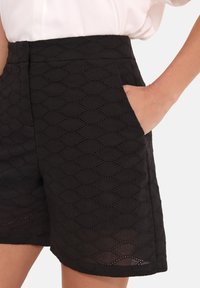 Czarne szorty wykonane z teksturowanej tkaniny z diamentowym wzorem, z elastycznym pasem i bocznymi kieszeniami, prezentujące finezyjne detale w formie wycięć.