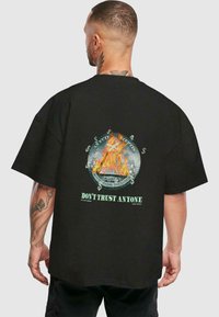 Black oversized t-shirt featuring a graphic design with flames, dollar signs, and the text "DON'T TRUST ANYONE" on the back.
