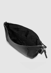 Schwarze Ledertasche mit Reißverschlussöffnung, ausgestattet mit einer strukturierten Außenseite und einem glatten Innenfutter. Enthält eine kleine Innentasche.
