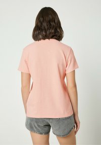 Short-sleeve, light pink t-shirt with a textured surface, round neckline, and relaxed fit, paired with grey denim shorts.