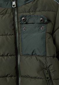 Gevoerde groene jas met een rits aan de voorkant, een gestructureerde borstzak met drukknoopsluiting en contrasterende stoffendetails.