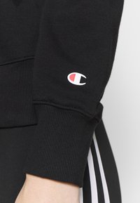 Zwart sweatshirt gemaakt van katoen, met geribbelde manchet en een klein wit-rood logo op de mouw. Glad oppervlak, sportief ontwerp.