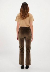 Pantalons en velours côtelé marron à taille haute et évasés, avec des poches arrière et une texture lisse. Associés à une chemise beige à manches courtes.