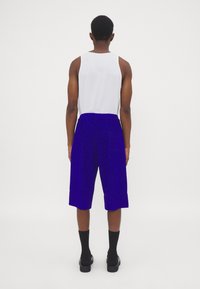 Blauwe shorts met een losse pasvorm, voorzien van een zichtbare tailleband en opgerolde uiteinden. Gepaard met een witte tanktop en zwarte sokken.