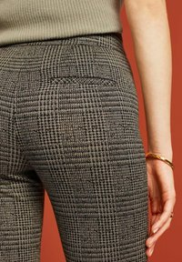Zwart-witte geblokte high-waisted broeken met een gestructureerde afwerking, voorzien van een achterzak en een aansluitende pasvorm. Accent van een gouden armband.