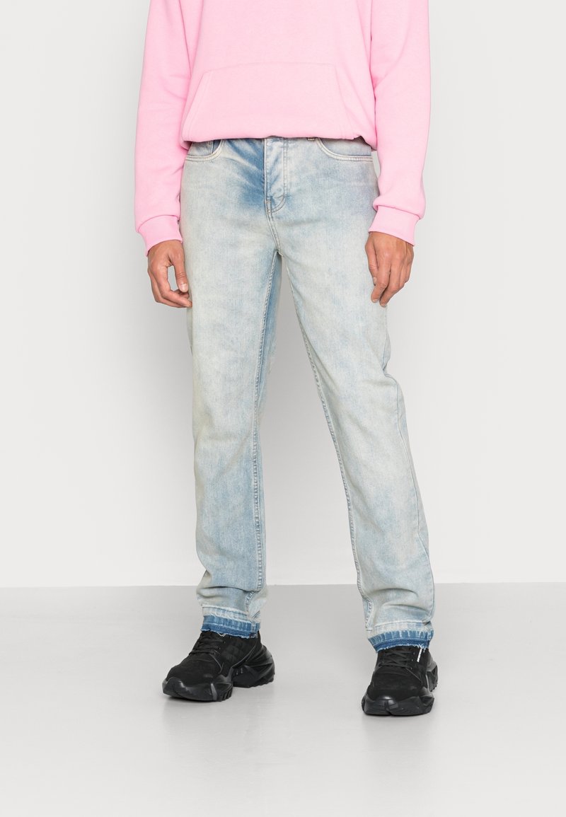 Jeans de un azul claro desvaído con un diseño de pierna recta, que cuentan con un clásico diseño de cinco bolsillos y una textura de tela desgastada. Combinados con zapatillas negras.