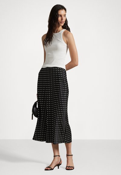 White ribbed tank top paired with a black polka-dot midi skirt. The skirt features a flared hem and is complemented by black strappy sandals and a small bag.