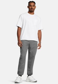 Weiße Baumwoll-T-Shirt mit kurzen Ärmeln und einer Brusttasche, kombiniert mit grauen Stretch-Hosen mit schmalem Schnitt und elastischen Bündchen.