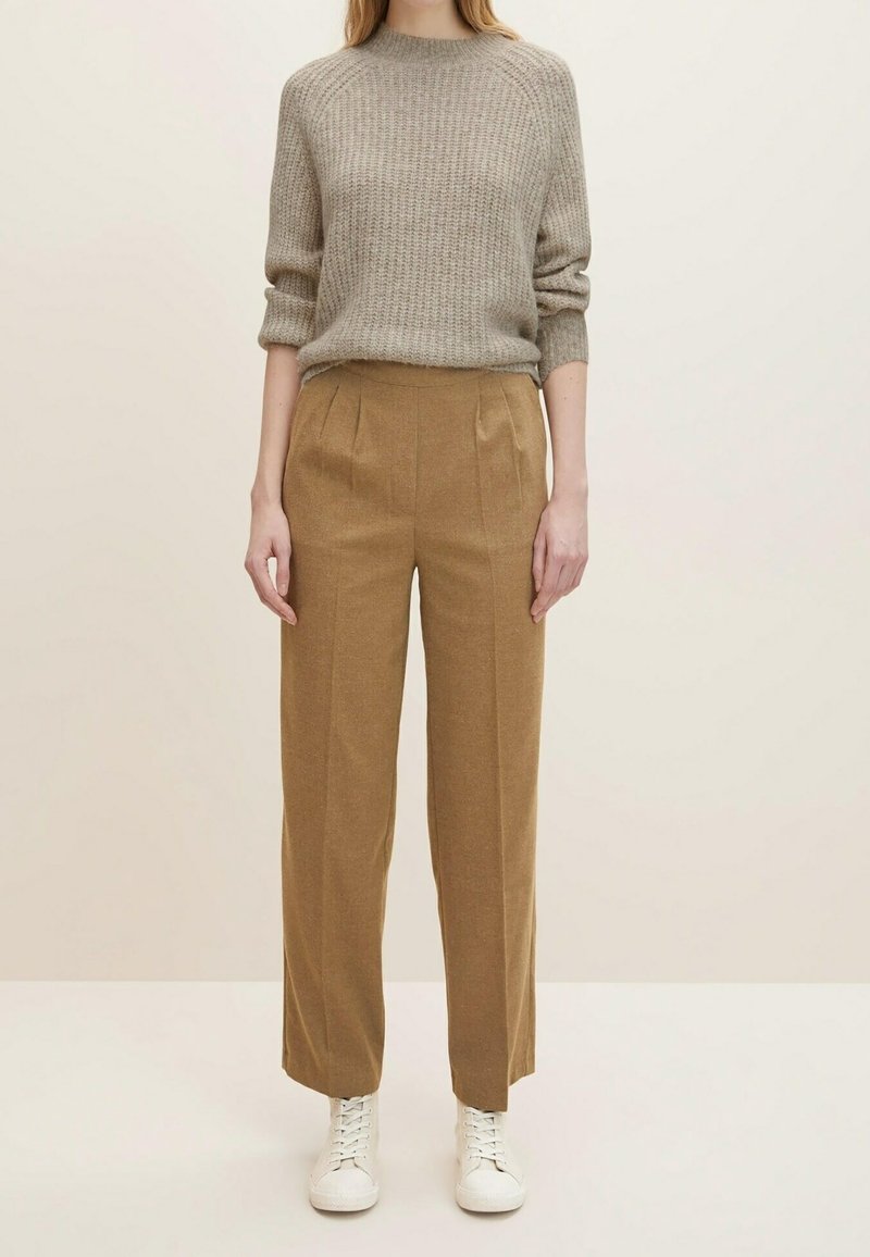 Pull gris clair à côtes, pantalon plissé couleur sable, et baskets blanches. La tenue présente des formes décontractées et des textures douces pour un style casual.