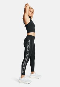Completo activewear nero composto da un top corto aderente e leggings a vita alta con una stampa geometrica bianca lungo il lato. Scarpe da ginnastica bianche.