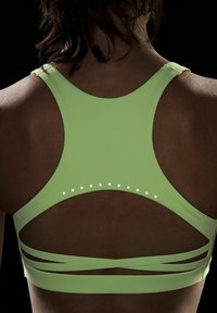 Neon zöld sportmelltartó, racerback megoldással, kivágott részletekkel és dekoratív fényvisszaverő pöttyökkel a hátsó pánt mentén.