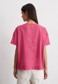 Roze top met korte mouwen, met een losse pasvorm, ronde halslijn en nette stiksels. De stof lijkt licht en glad. Gezien vanuit de achterkant.