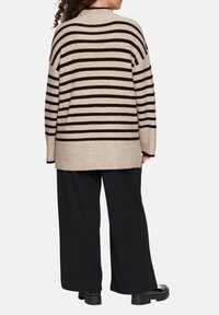 Beige en zwart gestreepte oversized trui, gebreide textuur, drop shoulders en lange mouwen. Draag met ruime zwarte broeken en dikke zwarte schoenen.