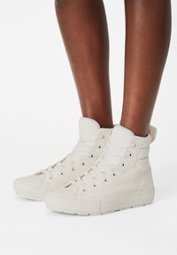 Baskets montantes en cuir blanc cassé avec lacets, col rembourré et semelle en caoutchouc. Comprend des coutures et un embout texturé.