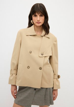 Abrigo beige de doble botonadura con grandes botones, amplio cuello y corte entallado. Tejido texturizado, bolsillos laterales y puños con cinturón.