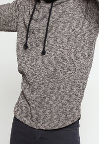 Harsoharmaa huppari, joka on valmistettu pehmeästä kankaasta ja jossa on naruilla säädettävä huppu sekä pyöristetty helma rentoa istuvuutta varten.