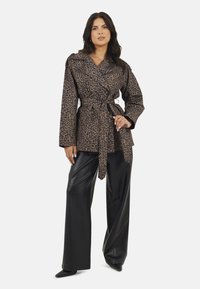 Kurtka w zwierzęcy wzór w panterę z wyraźnym kołnierzem i paskiem, zestawiona z czarnymi spodniami z ekoskóry o wysokim stanie. Powierzchnia o jedwabistym połysku.