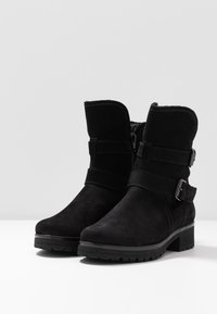 Botines de ante negro con un ligero tacón elevado, que presentan correas y hebillas en los laterales, y un suave forro interior.