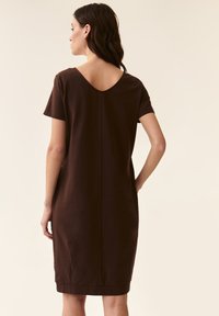 Brown short-sleeve dress with a V-shaped back neckline. Smooth fabric, knee-length, and a minimalistic design without patterns or embellishments.