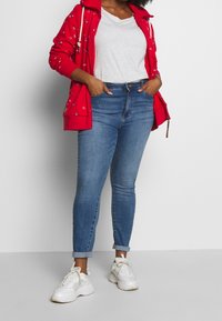 Czerwona bluza z kapturem na zamek z kwiatowym wzorem, szary t-shirt, niebieskie obcisłe dżinsy, białe tenisówki z jasnymi akcentami. Dżinsy podwinięte przy kostkach.