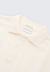 Crème-kleurig polo shirt met korte mouwen, gemaakt van biologisch katoen, met een opstaande kraag, knoopsluiting en een subtiele textuur in de stof.