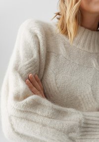 Maglione lavorato a maglia color crema con colletto alto, caratterizzato da un motivo a onde testurizzato e polsini a costine. Aspetto morbido, leggero e accogliente.