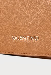 Texture di pelle color cuoio con finitura a granulato, caratterizzata dal logo dorato "VALENTINO". Il dettaglio del bordo cucito migliora il design.
