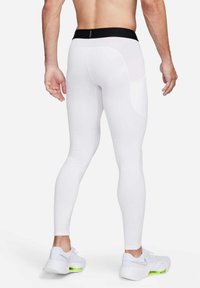 Leggings sportivi bianchi con una fascia nera in vita, caratterizzati da una texture liscia e un design aderente. Indossati con sneakers bianche, che mostrano un vivace accento verde.