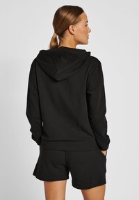 Svart huvtröja i mjukt tyg med en känguruficka, ribbade ärmslut och nederkant; matchas med svarta shorts.