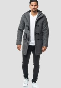 Abrigo de duffle gris con capucha, que presenta cierres de tipo toggles, bolsillos laterales y un diseño de mezcla de lana texturizada, combinado con vaqueros skinny negros y zapatillas.